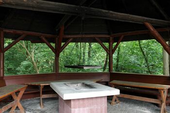 Innenansicht der Grillhütte mit Tischen, Holzbänken und gemauertem Grill