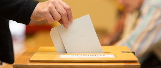 Eine Hand wirft den Stimmzettel in die Wahlurne